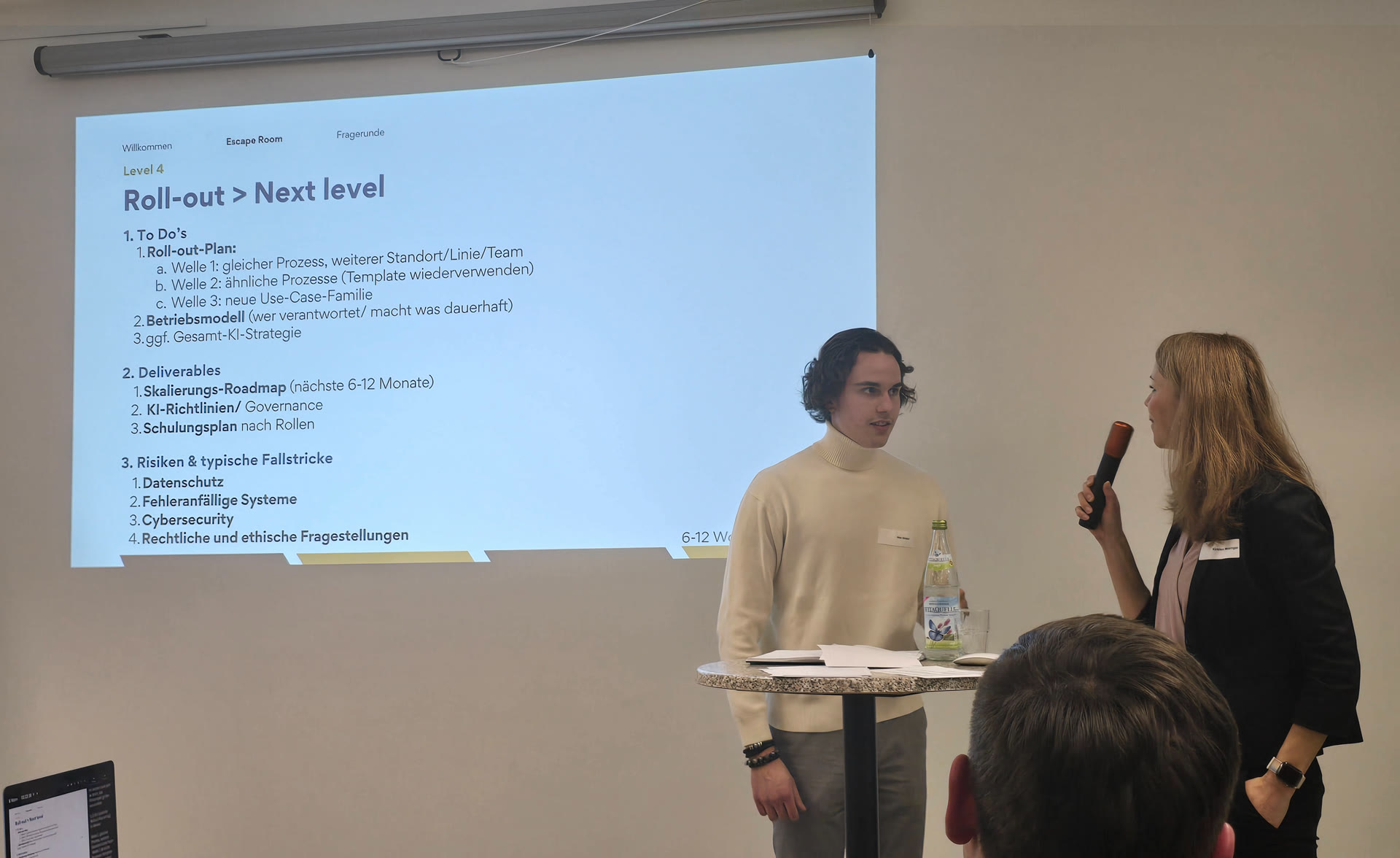 Nils Söder und Kirsten Meisinger beim KI Escape Room — Roll-out-Slide im Hintergrund