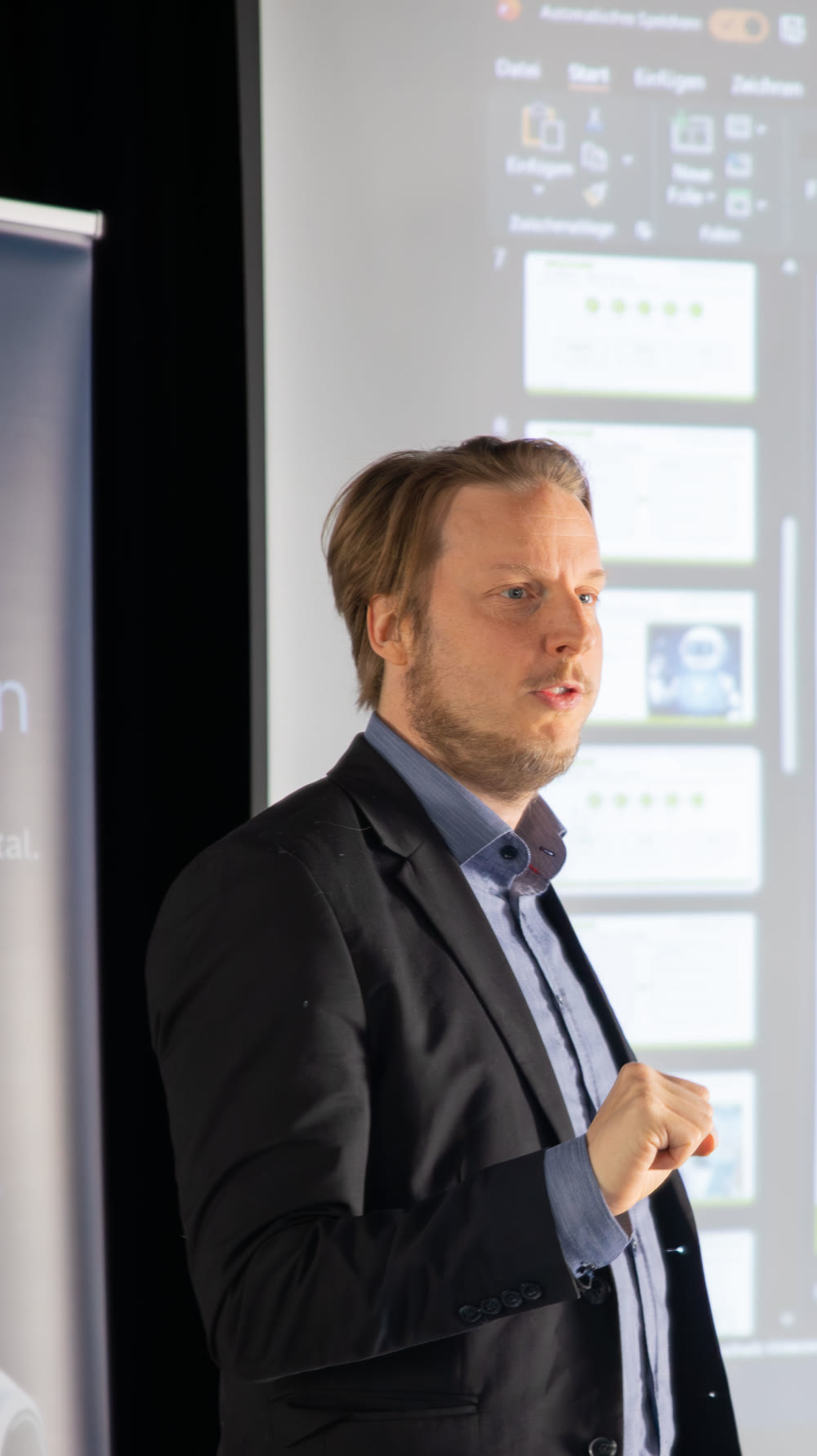 Florian Ludwig im Vortrag, Profilaufnahme — gestikulierend, im Hintergrund Auxdata-Banner und Vortragsfolien