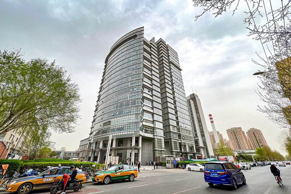 Geschwungenes Hochhaus mit Glasfassade an einer Straße in Peking, davor Taxis