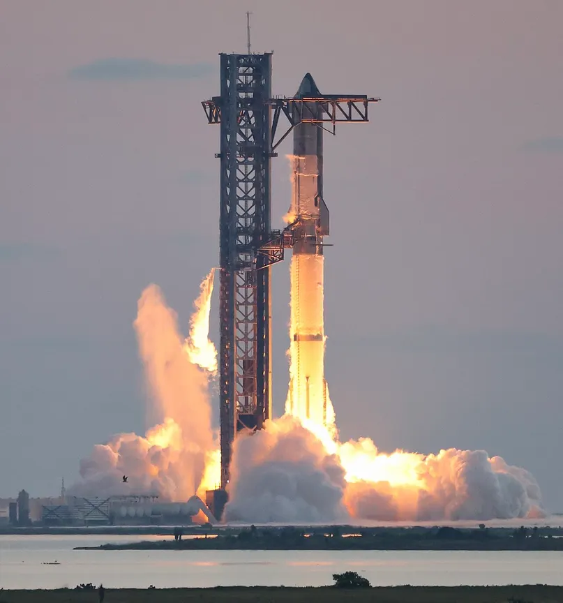 Starship-Rakete hebt neben dem Startturm ab, Flammen und Dampfwolken am Boden