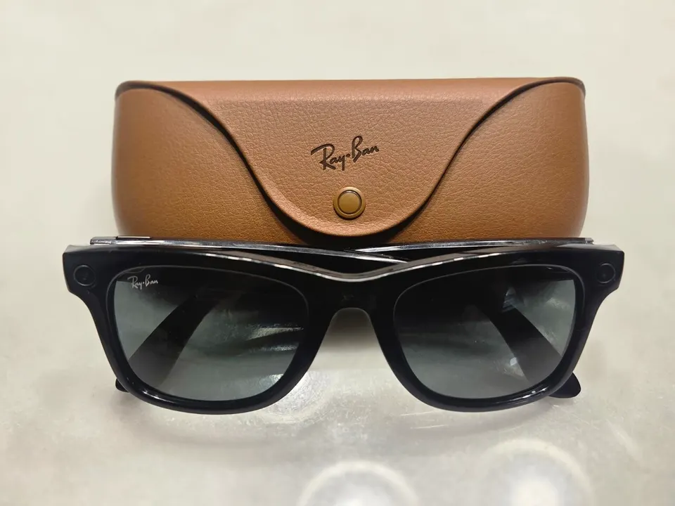 Schwarze Sonnenbrille mit Kameralinse am Rahmen vor einem braunen Lederetui mit Ray-Ban-Schriftzug