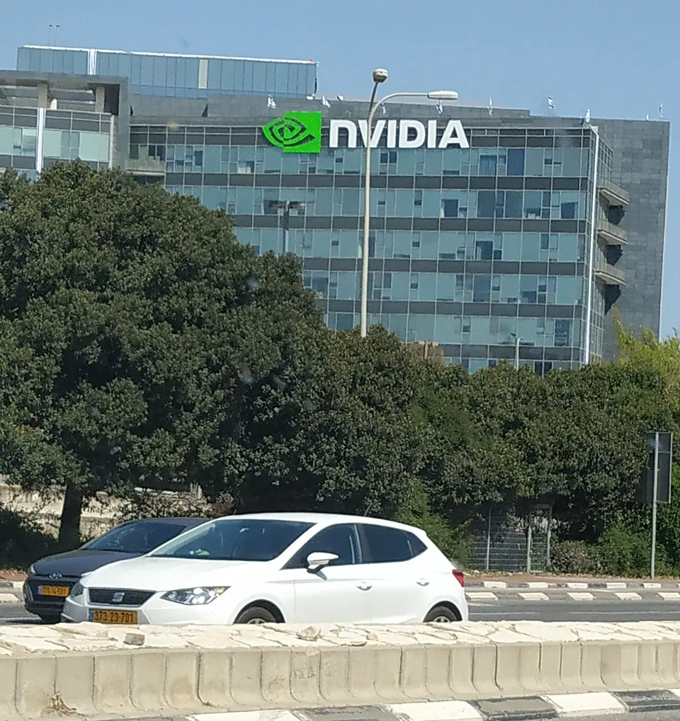 Bürogebäude mit NVIDIA-Schriftzug hinter Bäumen, davor ein weißes Auto