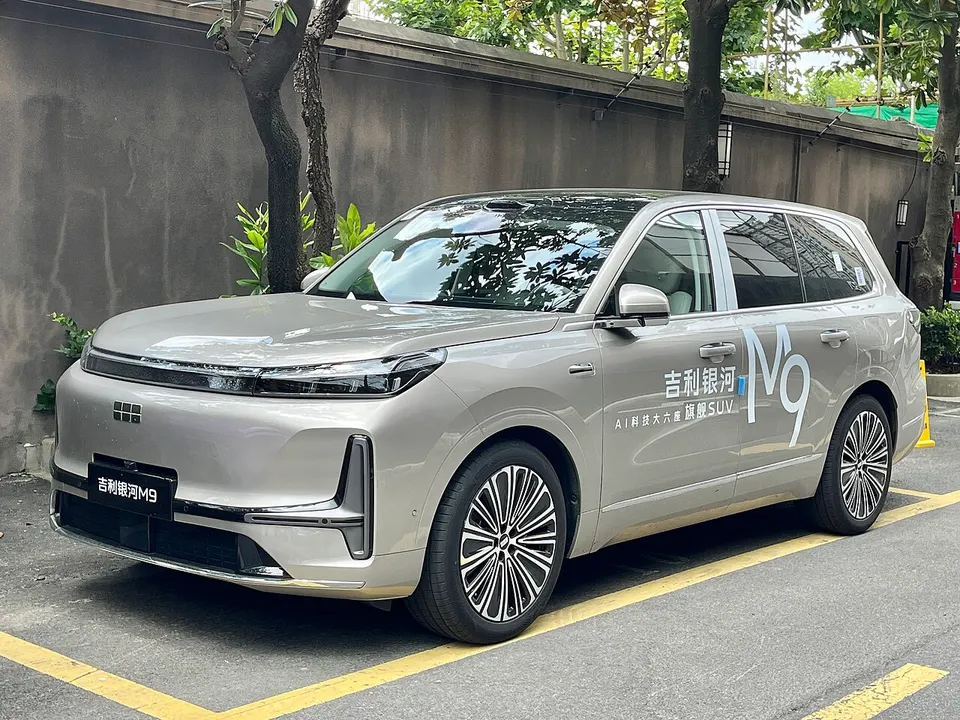 Silberner Geely-SUV mit der Aufschrift Galaxy M9 an der Seite, geparkt vor einer grauen Mauer