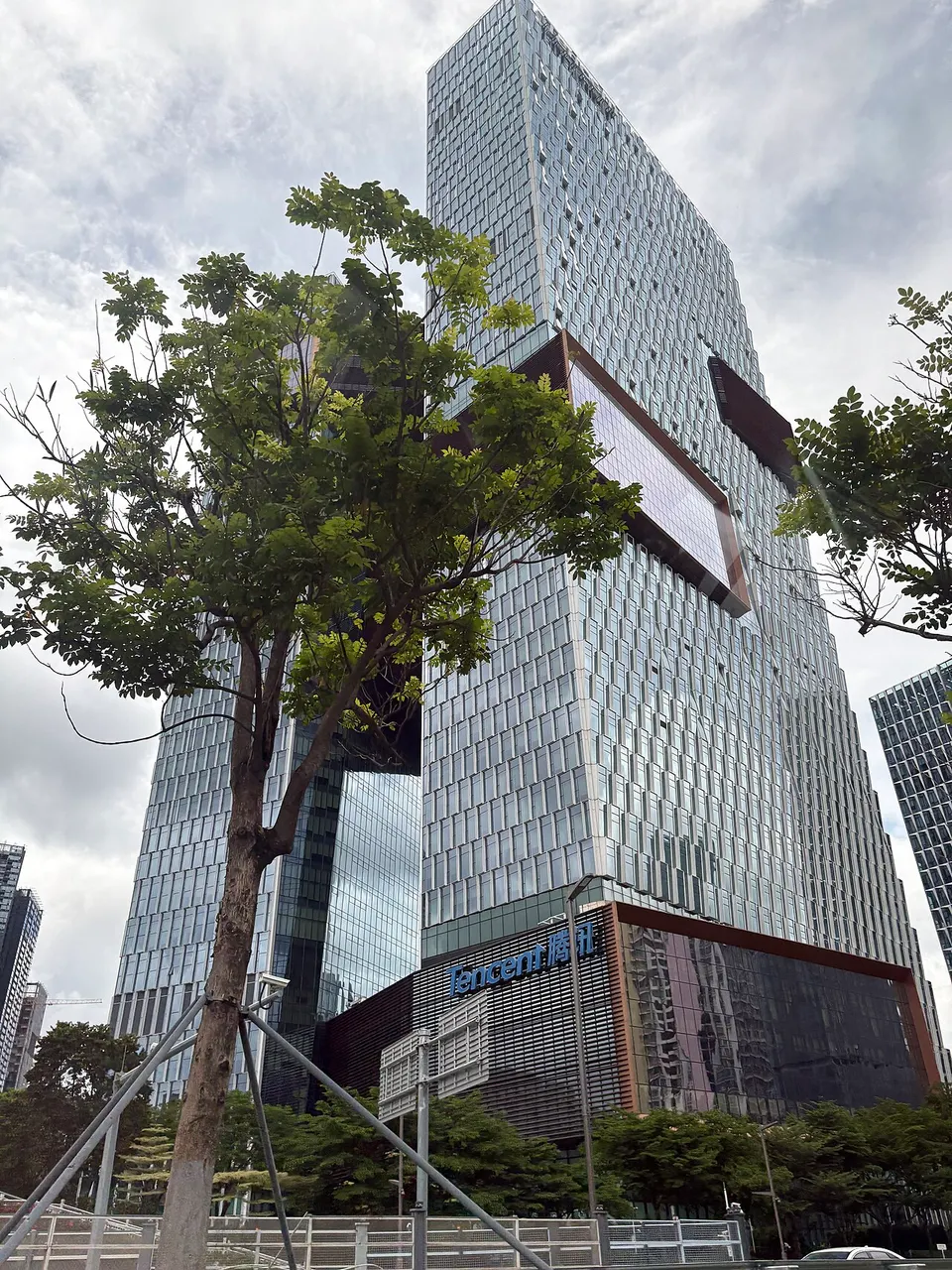 Zwei Glastürme, durch Brücken verbunden, davor ein Baum und am Sockel der Schriftzug Tencent