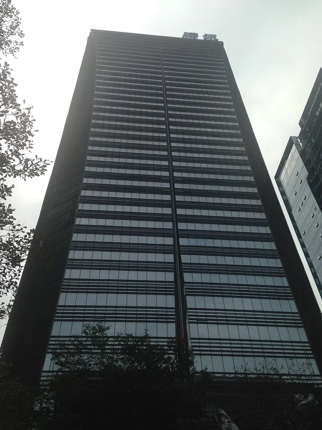 Dunkles, schmales Hochhaus mit Glasfassade, von unten fotografiert, oben ein Schriftzug