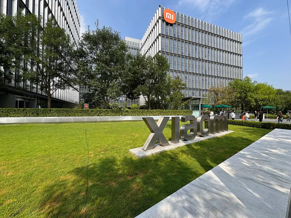 Glasfassaden-Bürogebäude mit orangem Mi-Logo, davor ein Rasen mit großen Metallbuchstaben „xiaomi“